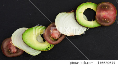 chopped vegetables black tomatoes, avocado and onions against black stone board 136620655