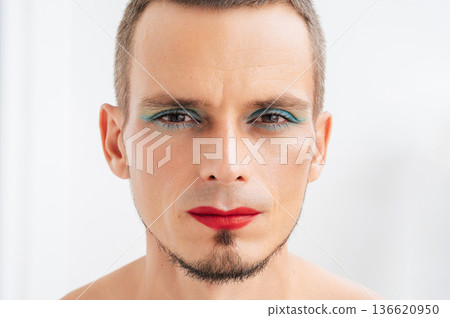 portrait of bearded gay man with makeup and cosmetics on face. A handsome transgender male with red lipstick and eye shadow sparkle on eyes on white background portrait of bearded gay man with makeup and cosmetics on face. A handsome transgender male with red lipstick and eye shadow sparkle on eyes on white background 136620950