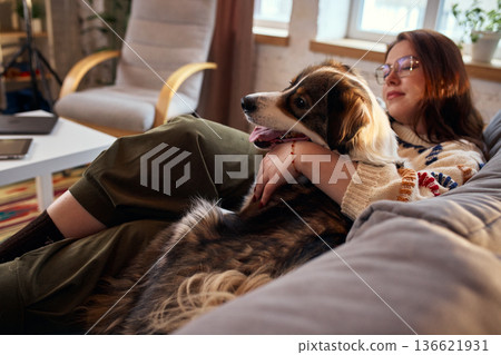 Woman resting on couch with dog in warm evening light. Woman resting on couch with dog in warm evening light. 136621931