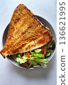 A bowl holds a large piece of fried fish resting on fresh salad with tomatoes, cucumbers, and lettuce. This healthy meal sits on a simple table surface 136621995