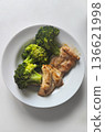 A plate contains grilled chicken pieces and steamed broccoli. The meal is placed on a plain white dish. It appears to be a healthy and nutritious option for lunch or dinner 136621998