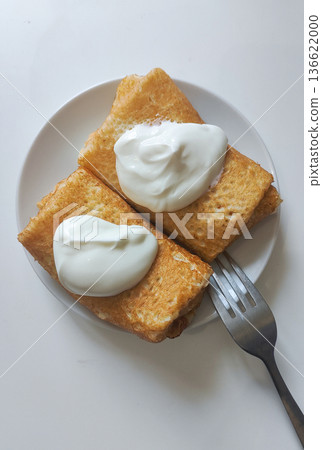 Two crepes filled with yogurt are placed on a white plate. A fork sits beside the plate. The setting suggests a simple breakfast time in a kitchen 136622000