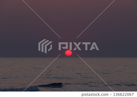 A tranquil sea view at dusk features a dark red sun A tranquil sea view at dusk features a dark red sun 136622067