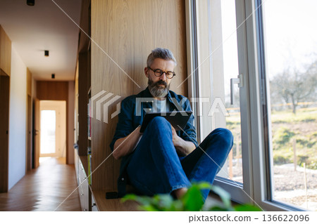 Man sitting by the window with tablet and writing notes. Man sitting by the window with tablet and writing notes. 136622096