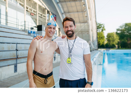 Portrait of coach with teen swimmer, standing by pool. 136622173