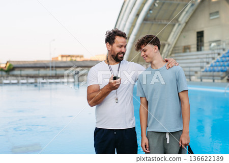 Coach giving advice to young swimmer, walking by pool. Coach giving advice to young swimmer, walking by pool. 136622189