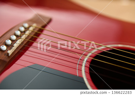 Close-up of a red acoustic guitar showing strings and bridge, illustrating adjusting and changing strings for guitar maintenance and repair practice and instrument care. Close-up of a red acoustic guitar showing strings and bridge, illustrating adjusting and changing strings for guitar maintenance and repair practice and instrument care. 136622283