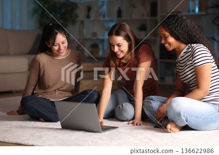 Three diverse happy friends checking laptop in the night Three diverse happy friends checking laptop in the night 136622986