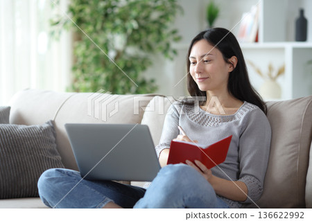 Asian woman cheking laptop and agenda at home Asian woman cheking laptop and agenda at home 136622992