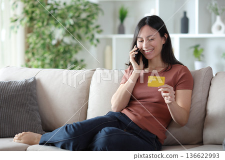 Happy asian woman calling on phone holding credit card Happy asian woman calling on phone holding credit card 136622993