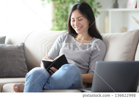 Happy asian woman taking notes in agenda at home Happy asian woman taking notes in agenda at home 136622998