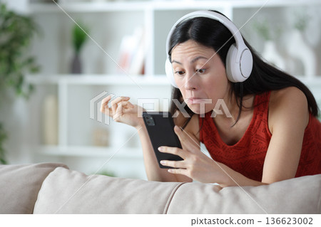 Perplexed asian woman checking media content on phone 136623002