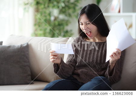 Excited asian woman reading check and letter at home Excited asian woman reading check and letter at home 136623008
