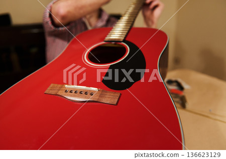 Red Acoustic Guitar Being Repaired and Strings Adjusted for Maintenance 136623129