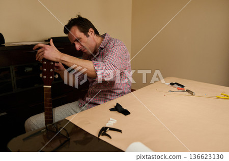 Man Adjusting Guitar Strings at a Table - Guitar Maintenance and Repair Man Adjusting Guitar Strings at a Table - Guitar Maintenance and Repair 136623130