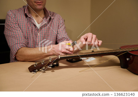 Man Changing Guitar Strings at Table - Guitar Maintenance and Repair Demonstration Man Changing Guitar Strings at Table - Guitar Maintenance and Repair Demonstration 136623140