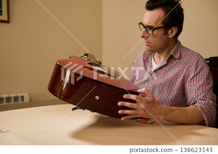 Man Adjusting Guitar Strings at Table - Master Guitar Maintenance and Repair Man Adjusting Guitar Strings at Table - Master Guitar Maintenance and Repair 136623143