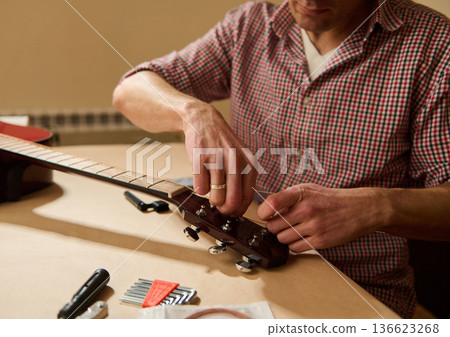 Man Adjusting Guitar Strings During Maintenance and Repair in Workshop Man Adjusting Guitar Strings During Maintenance and Repair in Workshop 136623268