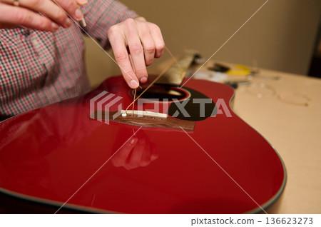 Person Changing Strings on Red Acoustic Guitar Repair and Maintenance Person Changing Strings on Red Acoustic Guitar Repair and Maintenance 136623273