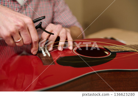Man Changing Guitar Strings on Red Acoustic Guitar Demonstrating Maintenance and Repair Technique 136623280