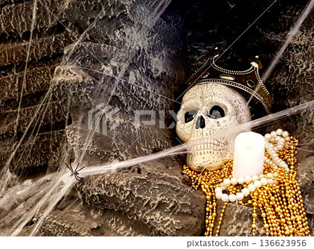 A human skull wearing a gold crown rests in a dark cave surrounded by thick cobwebs, a small spider, a white candle, and golden pearls. Spooky dungeon theme perfect for Halloween or gothic concepts. A human skull wearing a gold crown rests in a dark cave surrounded by thick cobwebs, a small spider, a white candle, and golden pearls. Spooky dungeon theme perfect for Halloween or gothic concepts. 136623956