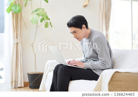 An Asian man hunched over while operating a computer 136624465