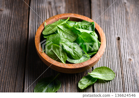 Bright leafy spinach arranged in wooden bowl on weathered wooden table Bright leafy spinach arranged in wooden bowl on weathered wooden table 136624546