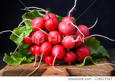 Close up of radish bunch on chopping board with dark moody background Close up of radish bunch on chopping board with dark moody background 136624567