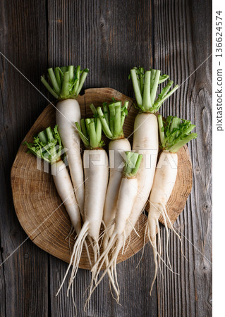 Daikon radish with green leaves on wooden cutting board Daikon radish with green leaves on wooden cutting board 136624574