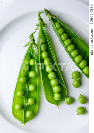 Fresh green peas in pods arranged on a white plate 136624589