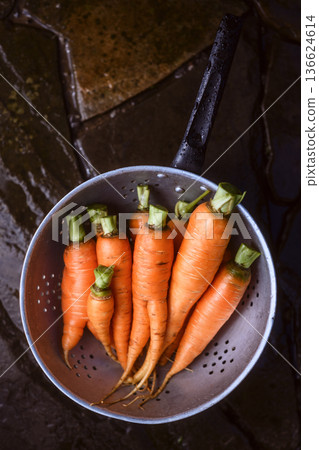 Freshly washed carrots with greens in metal colander 136624614
