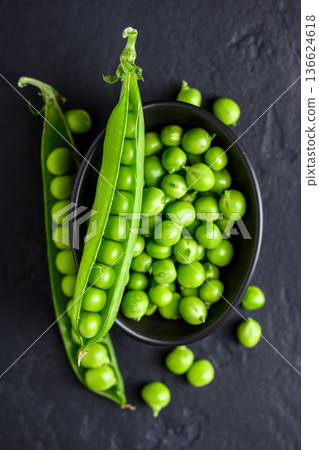 Green peas in black ceramic bowl with scattered pods 136624618
