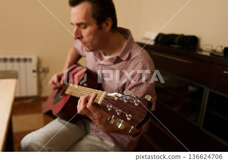 Man Adjusting Guitar Strings Indoors - Guitar Maintenance, Repair and Tuning Practice Man Adjusting Guitar Strings Indoors - Guitar Maintenance, Repair and Tuning Practice 136624706