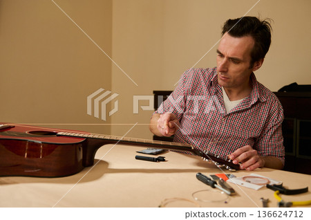 Man Replacing Guitar Strings at Table - Guitar Maintenance and Repair Man Replacing Guitar Strings at Table - Guitar Maintenance and Repair 136624712