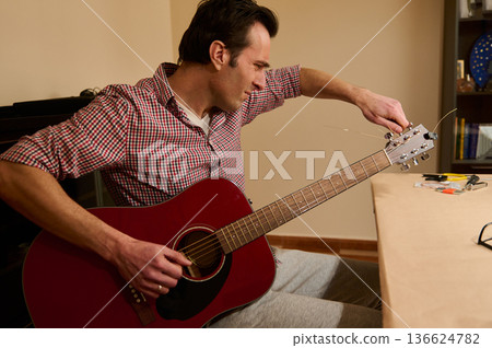 Man Adjusting Acoustic Guitar Strings While Tuning and Repairing at Home Man Adjusting Acoustic Guitar Strings While Tuning and Repairing at Home 136624782