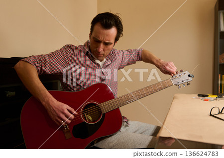Man Adjusting Guitar Strings At Home - Guitar Maintenance And Repair Practice Man Adjusting Guitar Strings At Home - Guitar Maintenance And Repair Practice 136624783