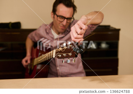 Man Changing Guitar Strings at Home - Guitar Maintenance, Repair and Tuning Man Changing Guitar Strings at Home - Guitar Maintenance, Repair and Tuning 136624788