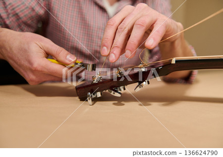Man Changing Guitar Strings On Headstock With Pliers - Guitar Maintenance And Repair Man Changing Guitar Strings On Headstock With Pliers - Guitar Maintenance And Repair 136624790
