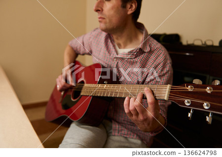 Man Adjusting and Changing Guitar Strings on Red Acoustic Guitar - Maintenance and Repair Practice Man Adjusting and Changing Guitar Strings on Red Acoustic Guitar - Maintenance and Repair Practice 136624798