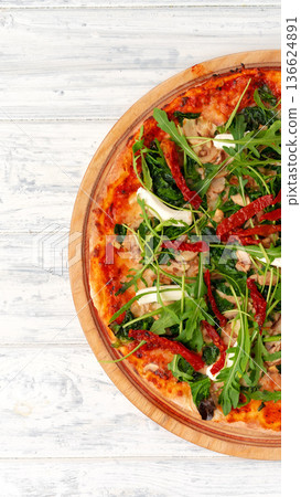 Pizza topped with greens and sun-dried tomatoes on wooden board at a restaurant 136624891
