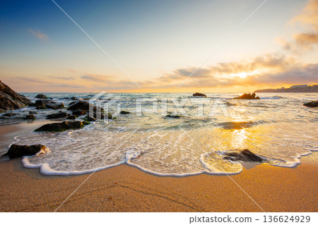 beautiful sunrise over empty sandy beach at the black sea. white foam rolling on to the shore near boulder. perfect summer vacation concept. awesome weekend from resort in sozopol. low angle 136624929