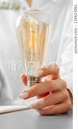 Holding a light bulb with glowing filaments in a bright room while working on a project 136624961