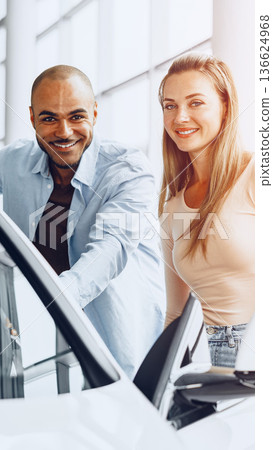 Two people smiling while examining a car in a dealership showroom during the day Two people smiling while examining a car in a dealership showroom during the day 136624968