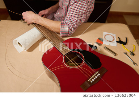 Man Changing Guitar Strings on Red Acoustic Guitar for Repair and Maintenance 136625004