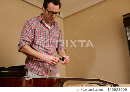 Man Changing Guitar Strings at Home Workshop - Guitar Maintenance and Repair Man Changing Guitar Strings at Home Workshop - Guitar Maintenance and Repair 136625006