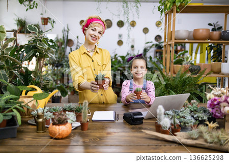 A woman and a young girl smile while holding potted plants in a plant shop A woman and a young girl smile while holding potted plants in a plant shop 136625298