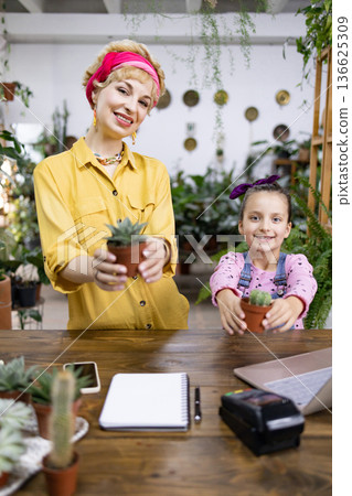 A woman and a young girl smile while holding small potted plants in a bright, inviting space A woman and a young girl smile while holding small potted plants in a bright, inviting space 136625309