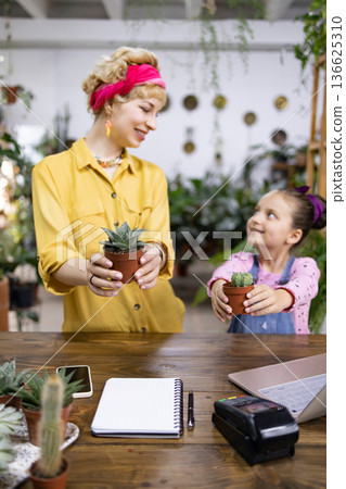 A mother and daughter share a moment while holding potted plants, creating a heartwarming scene A mother and daughter share a moment while holding potted plants, creating a heartwarming scene 136625310