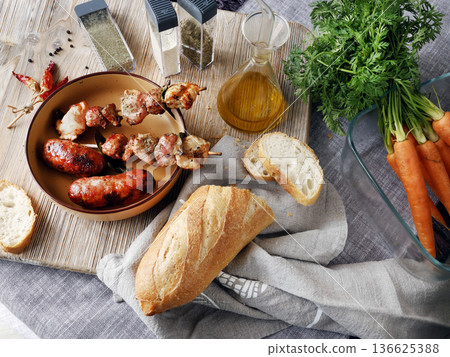 Composition of grilled sausages and pieces of meat on wooden skewer. Seasonal farm produce, vegetable, and bread. Homemade food. Designer background. 136625388