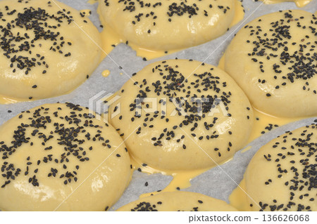 Raw burger buns with black sesame seeds on baking paper Raw burger buns with black sesame seeds on baking paper 136626068